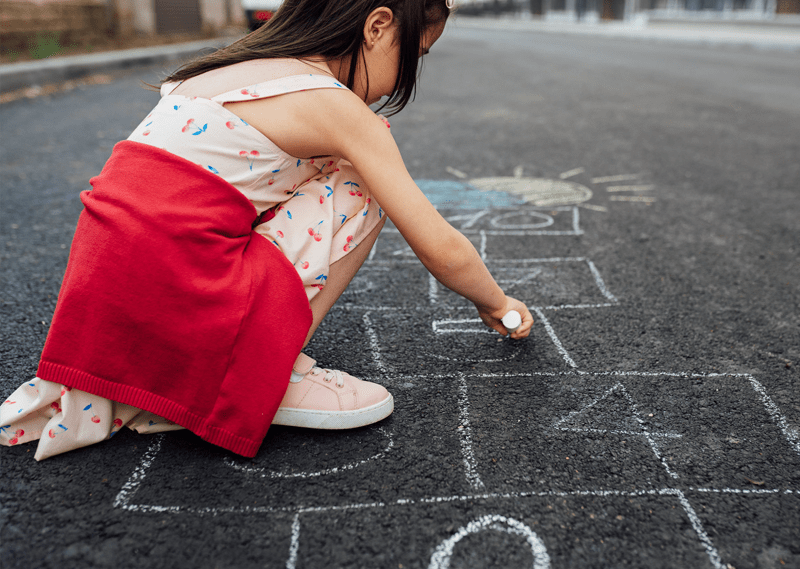 Girl drawing hopscotch on tarmac street